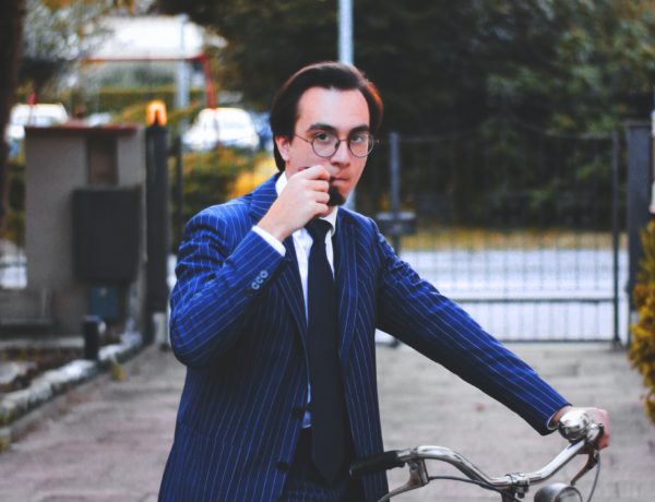 man in a suit riding bicycle during daytime while smoking a pipe